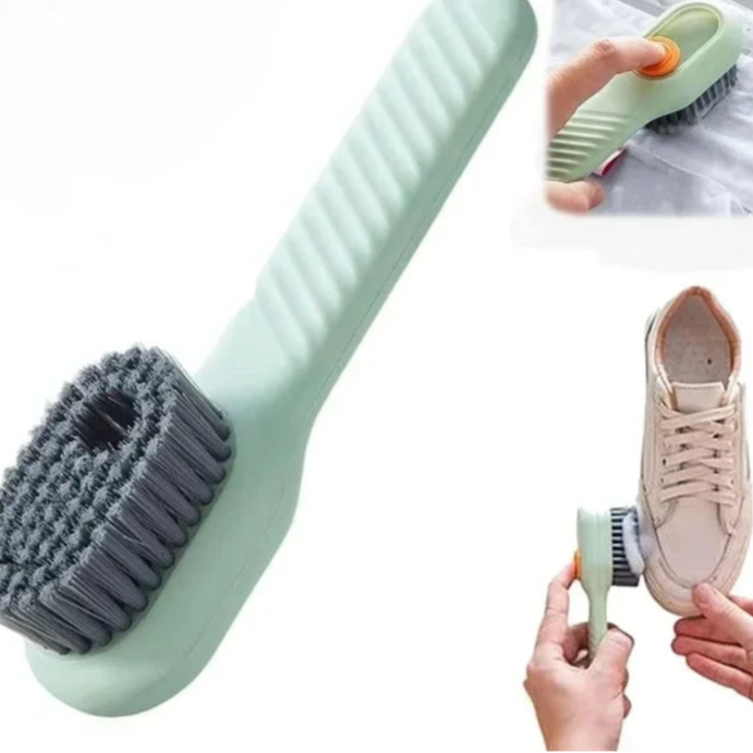 Cleaning brush with grey bristles and green handle, used on a white surface and a beige sneaker.