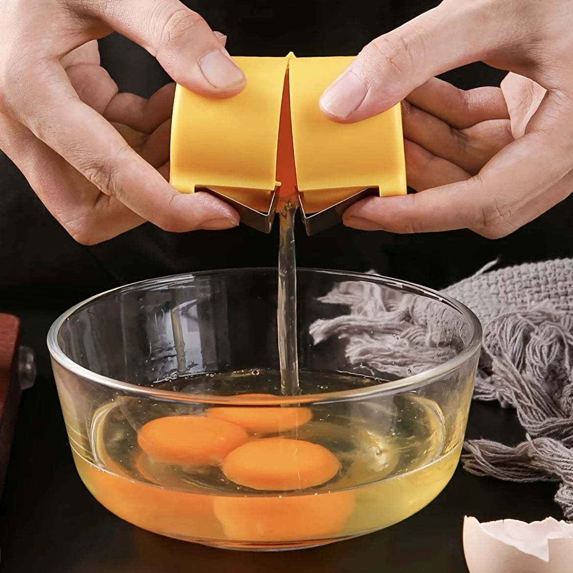 Person using a yellow egg separator to separate yolks into a glass bowl.