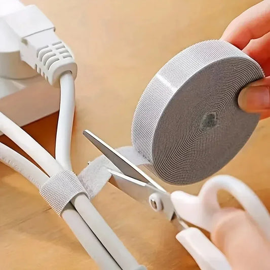 Person using scissors to cut grey cable tie around white cables on a beige surface
